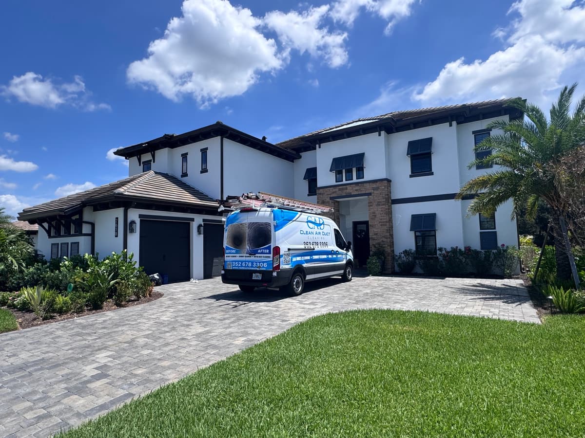 A Clean Air Duct Cleaning van in the driveway of a large two-story home