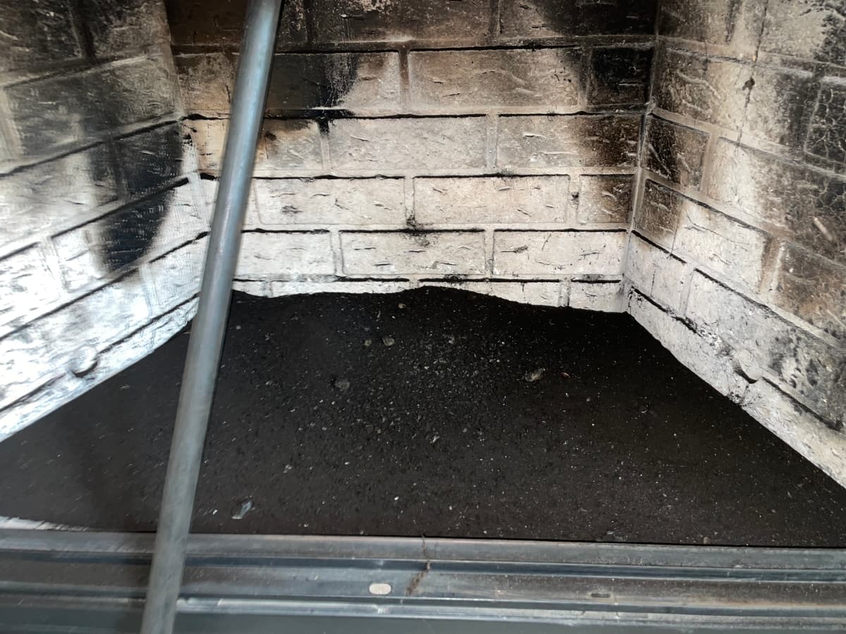 A fireplace firebox with soot on the brick walls during chimney cleaning