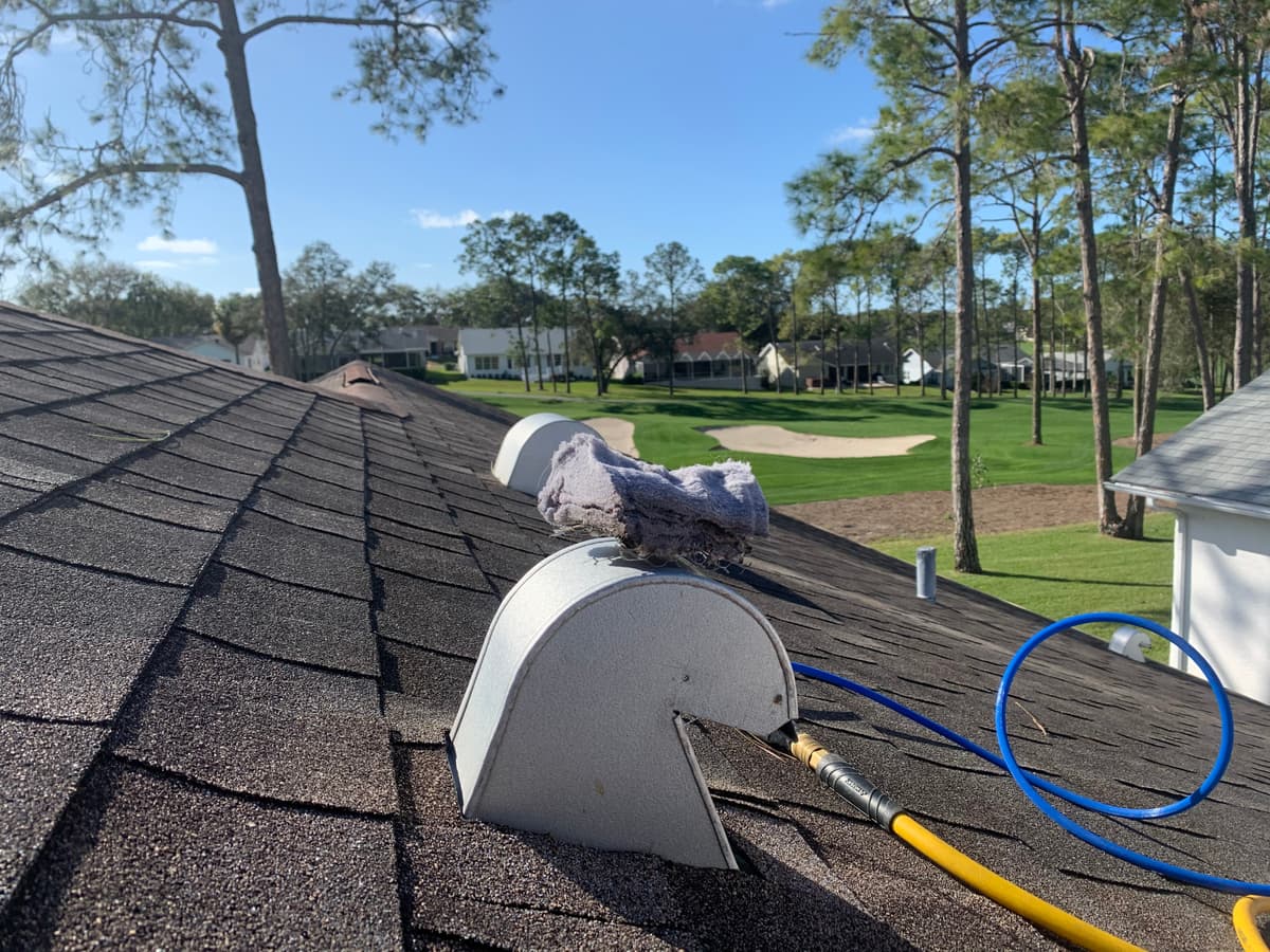 A dryer vent cleaning line running into a roof vent cap on a shingle roof
