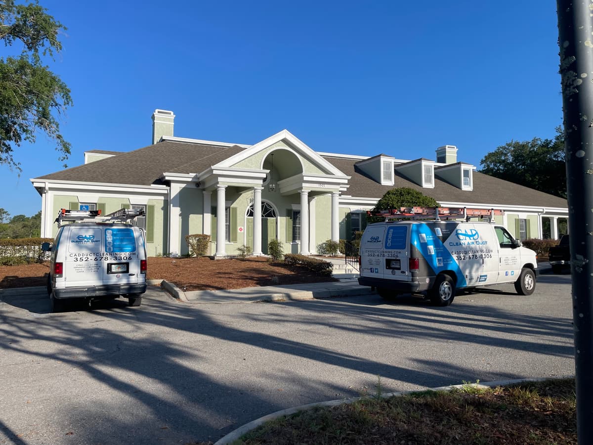 Clean Air Duct Cleaning vans parked outside a large clubhouse building for a commercial cleaning job