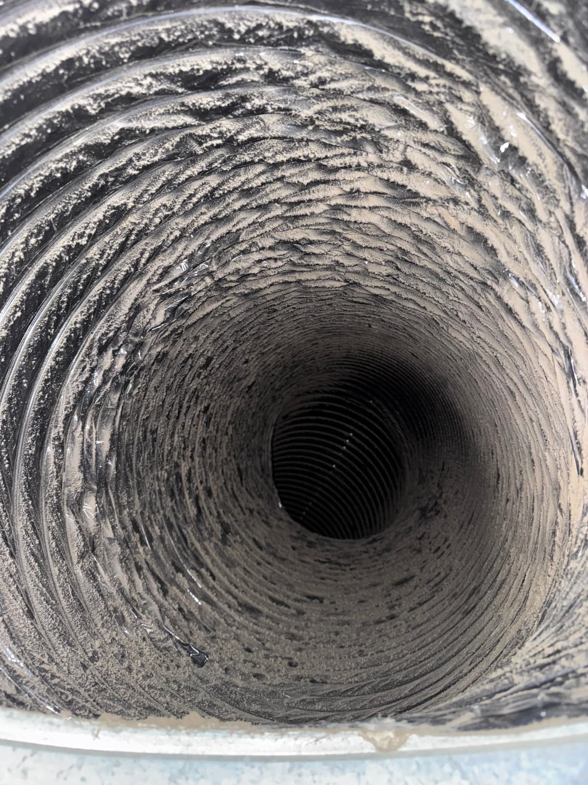 A flexible duct with heavy gray dust clinging to its ribs before cleaning