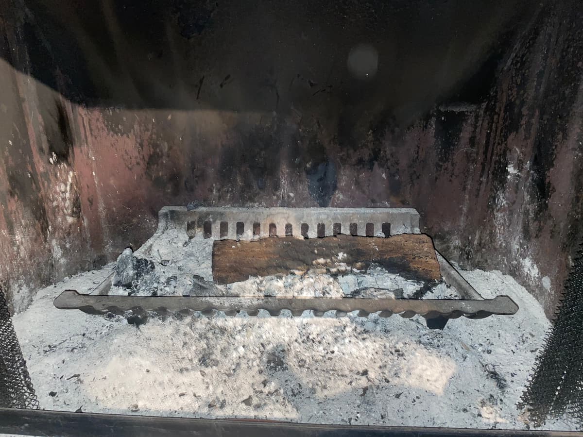Ash and a charred log on the grate of a fireplace before chimney cleaning