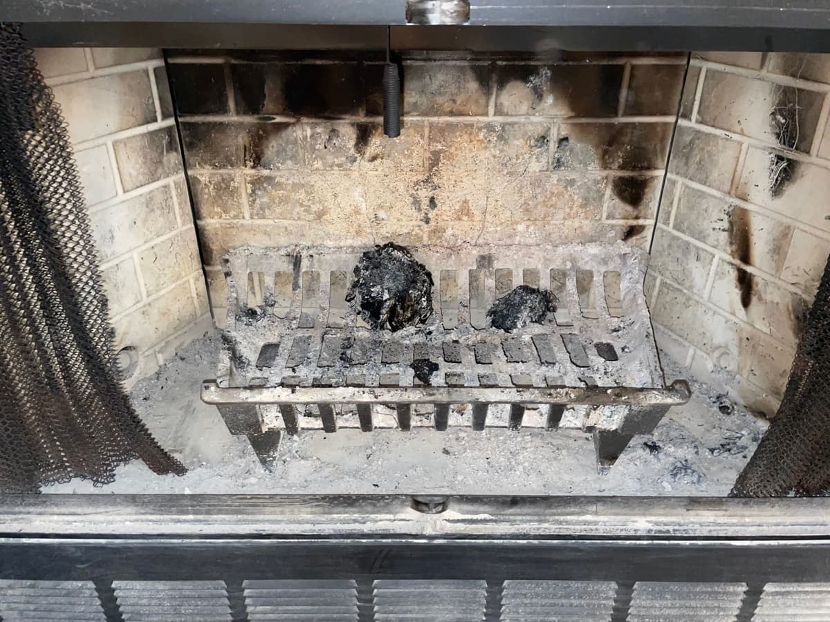 A fireplace with soot on the brick and ash under the grate before chimney cleaning