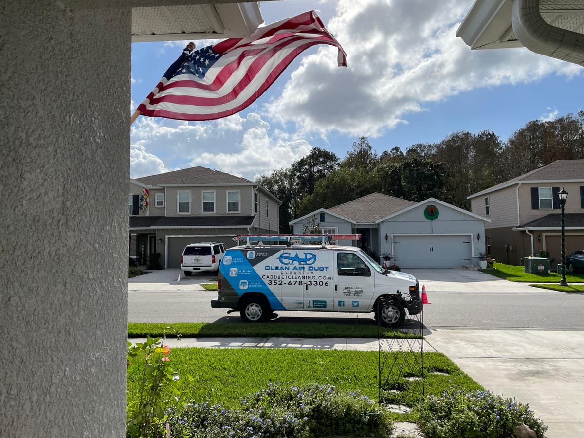 An American flag flying over a Clean Air Duct Cleaning van parked in a residential neighborhood