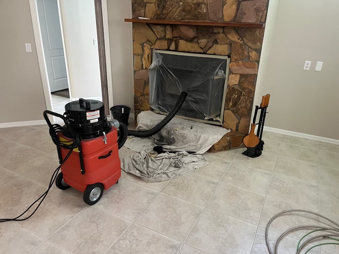 A chimney cleaning vacuum set up in front of a stone fireplace, with a drop cloth protecting the floor