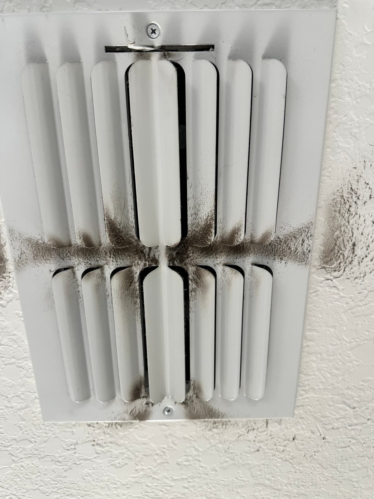 A ceiling supply register streaked with dust around its louvers