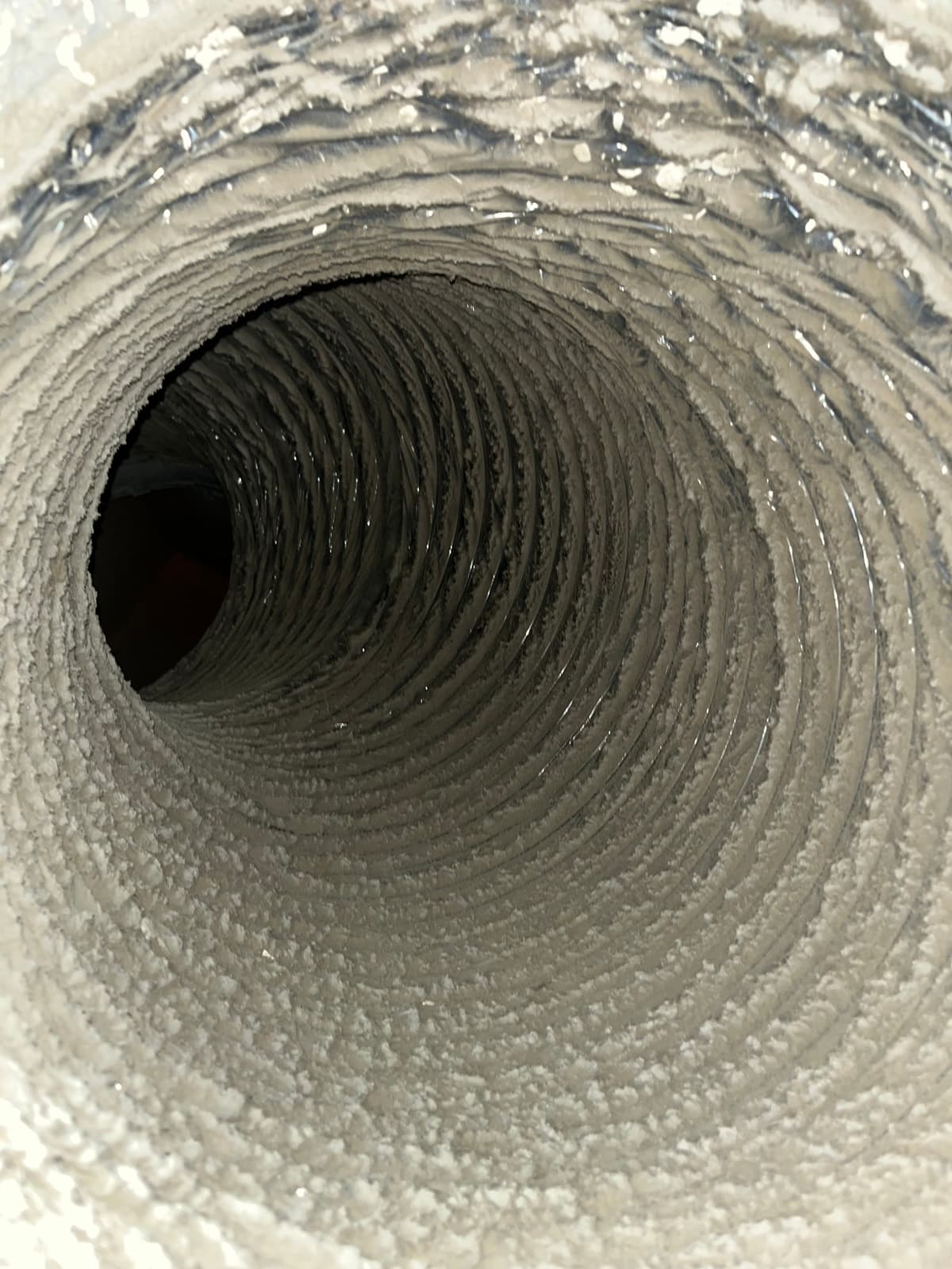 A flexible supply duct coated in thick tan dust before cleaning