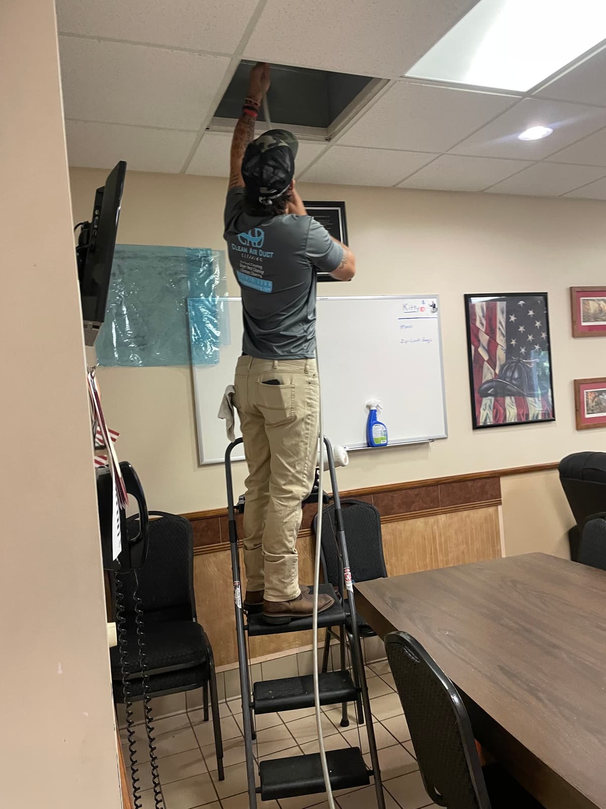 A Clean Air Duct Cleaning technician on a ladder cleaning air ducts in a Pasco County fire station