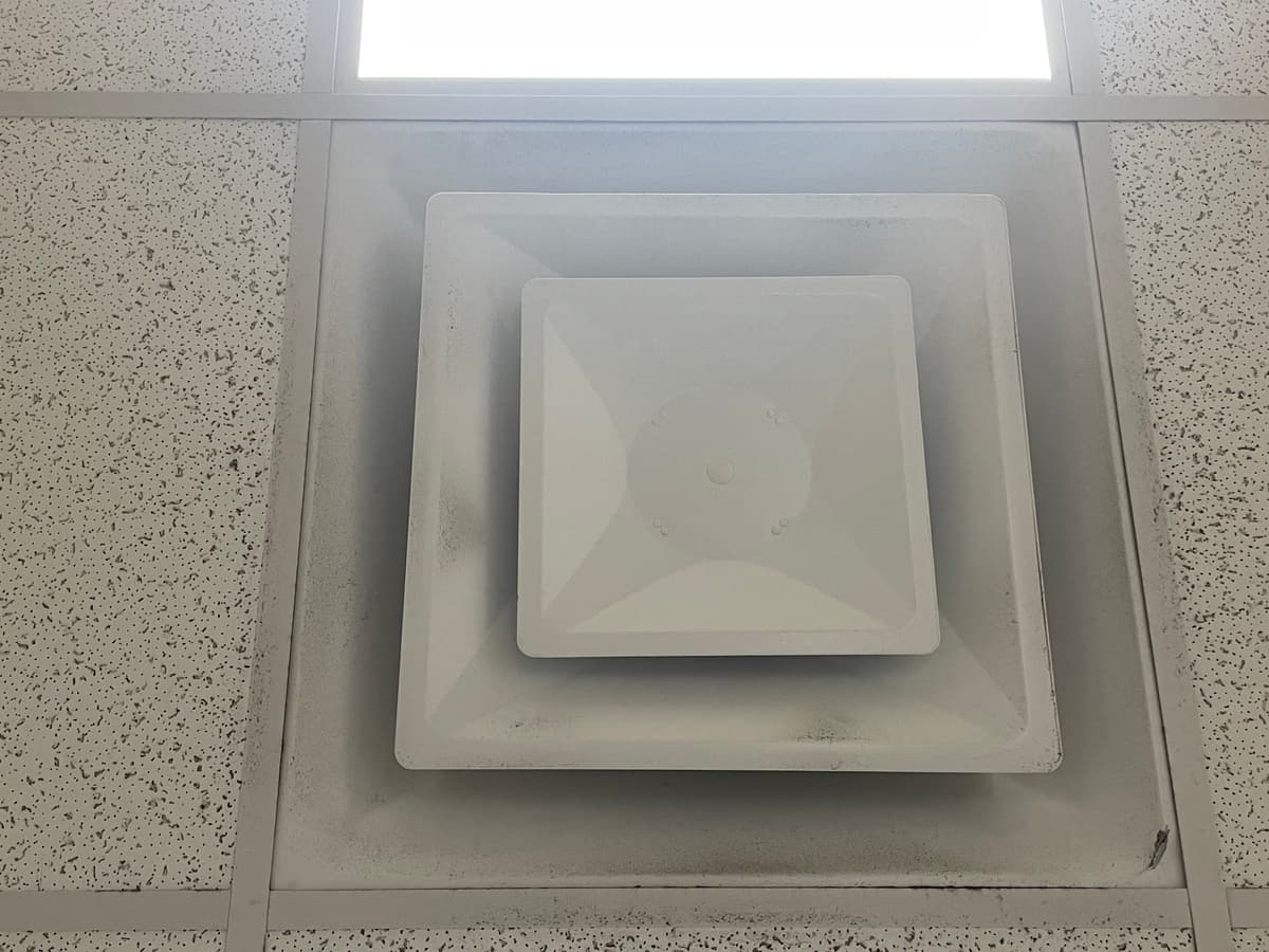 A square ceiling diffuser with dust around its edges before cleaning
