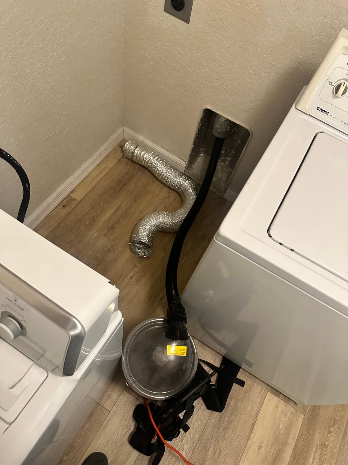 A dryer vent cleaning hose fed into the wall connection behind a dryer