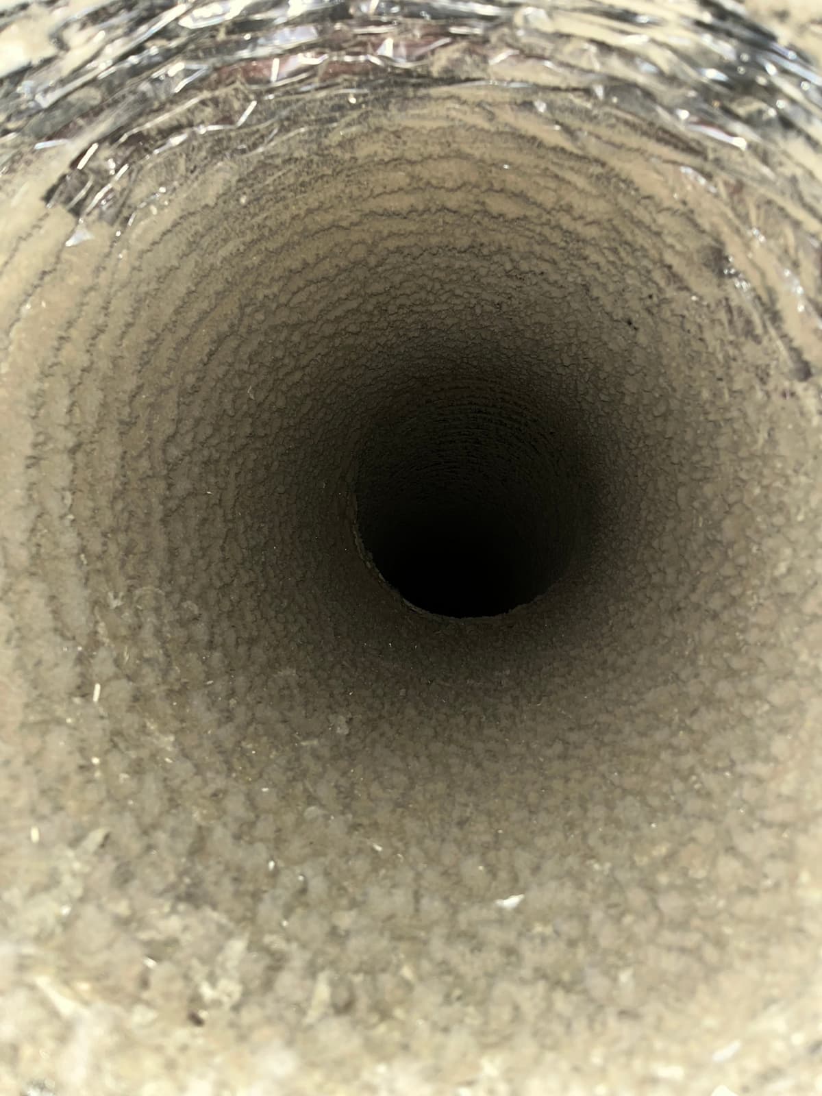A flexible duct lined with a thick layer of beige dust before cleaning