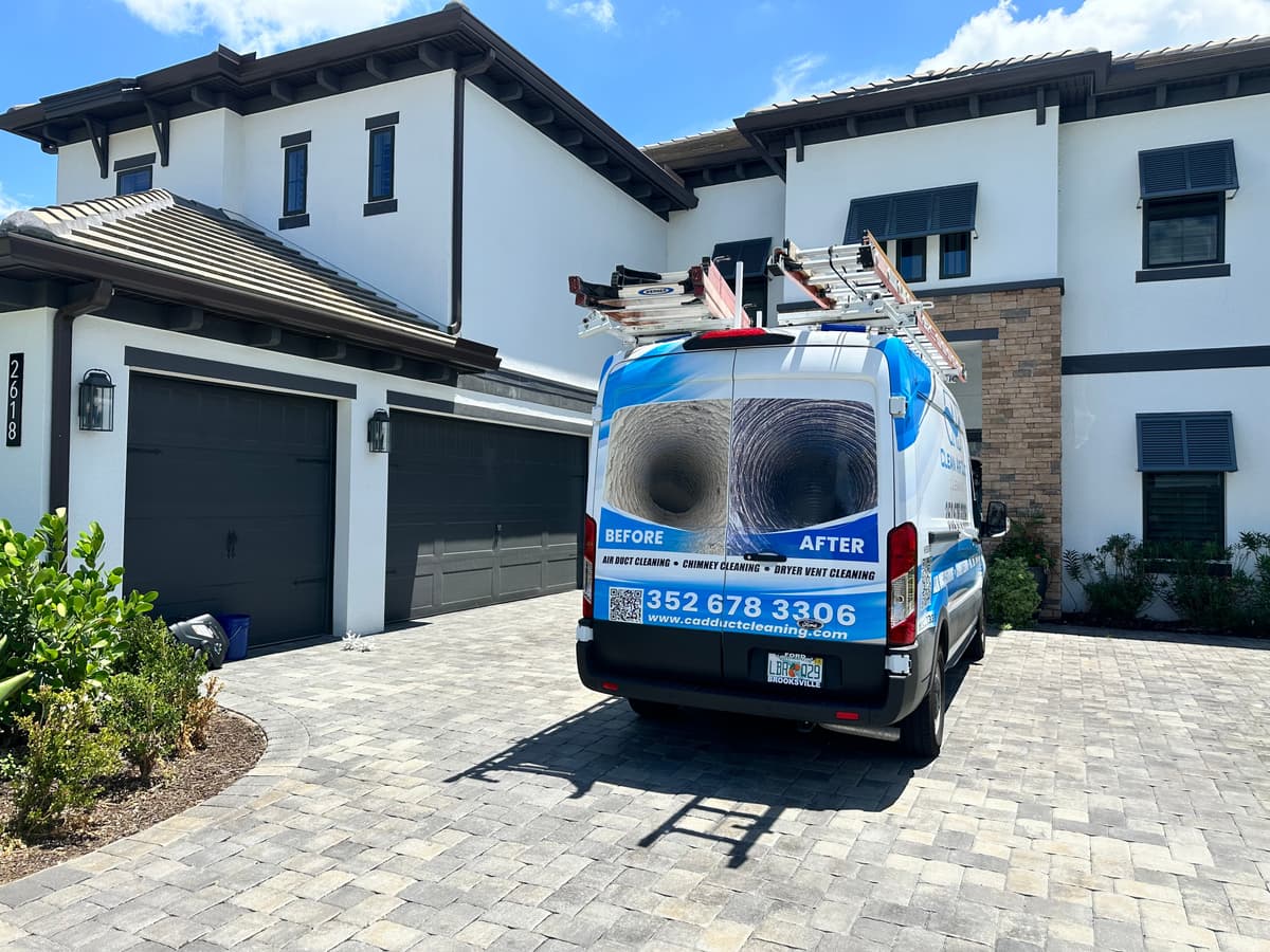 A Clean Air Duct Cleaning van parked on the paver driveway of a large two-story home