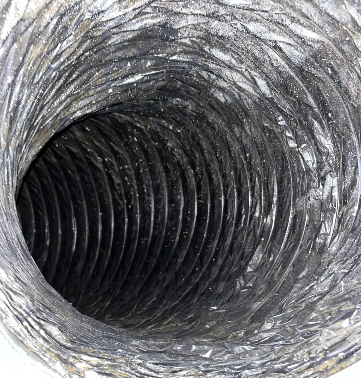 A long commercial exhaust run before cleaning, its liner darkened with compacted lint