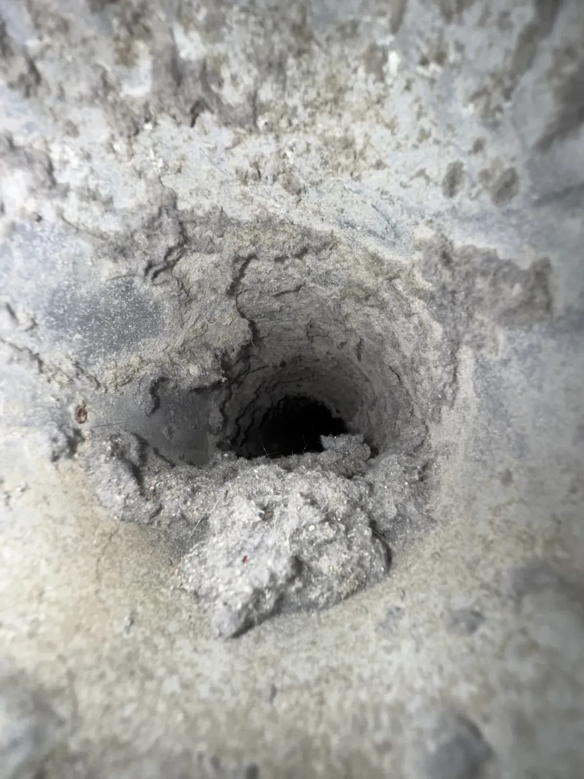 A commercial duct riser before cleaning, its opening narrowed by a thick collar of packed lint and dust