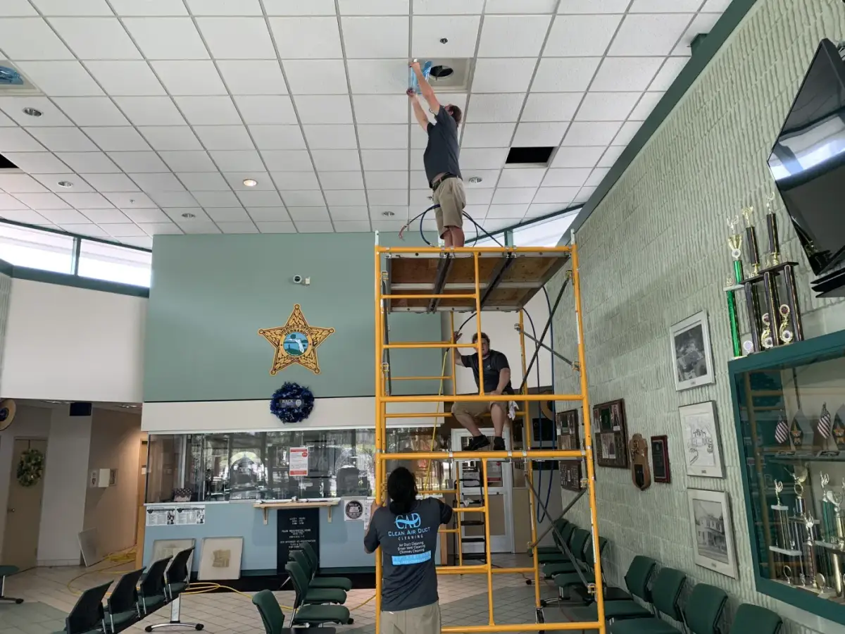 A technician on a ladder cleaning ceiling vents in an office
