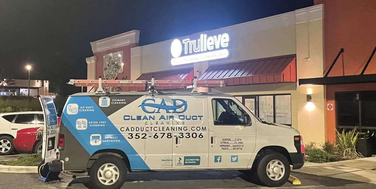 A Clean Air Duct Cleaning van working outside a Florida retail unit after closing, the shopfront lit behind it