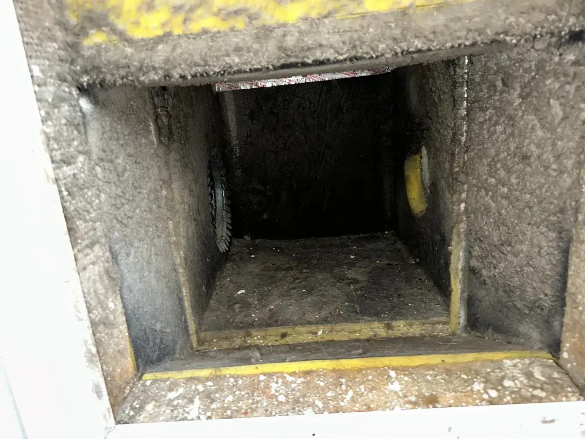 A metal duct boot behind a register, coated with dust