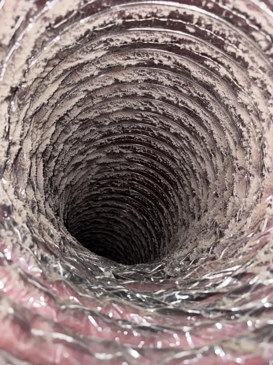 Looking down the inside of an uncleaned flexible air duct, its ribs packed with a thick grey coat of dust and lint