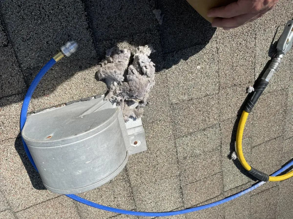 Lint cleared onto the roof beside a dryer vent and air line