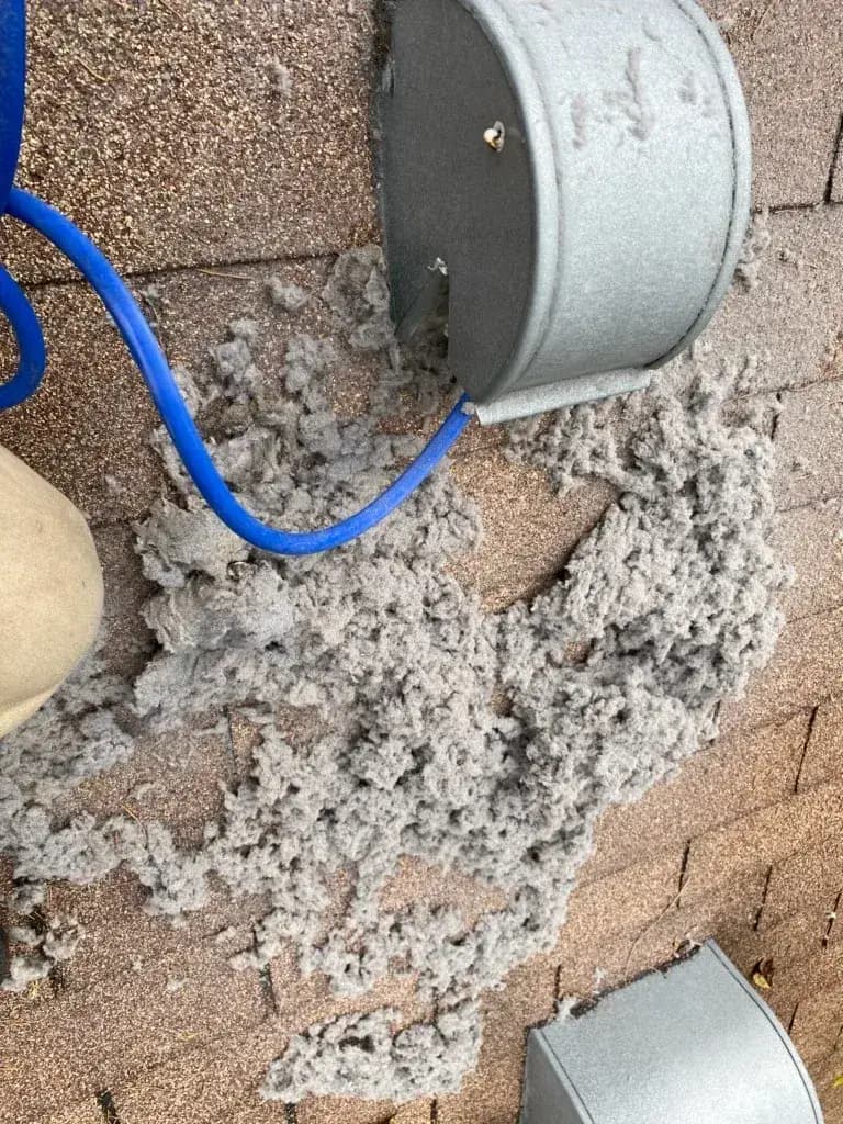 A pile of lint beside a roof dryer vent during cleaning