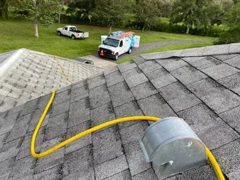 A dryer vent cap on a roof with the cleaning hose in place