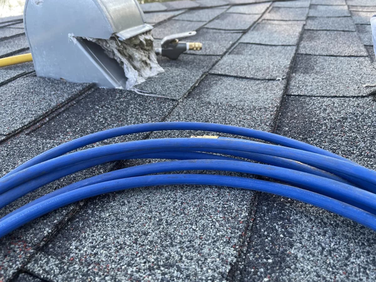 Compressed-air lines running across a roof to a dryer exhaust hood packed with lint, mid-clean