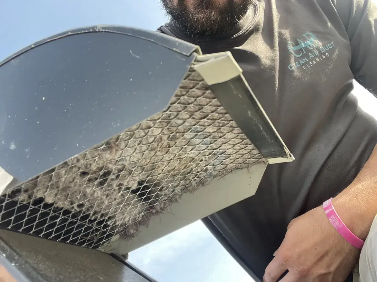 A technician holding a dryer vent screen matted with lint