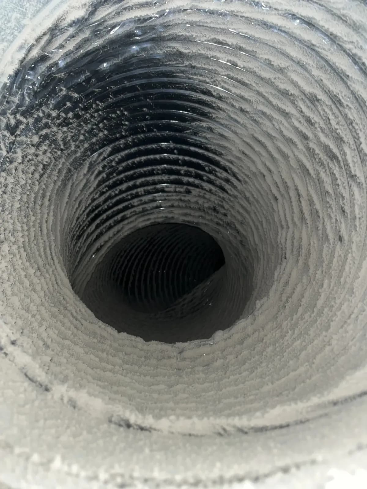 A duct run on the blower side of an air handler, its liner thick with the fine dust a loaded fan wheel throws