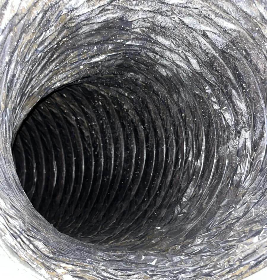 The inside of an air handler connection darkened with the fine, greasy fouling that collects downstream of a dirty coil