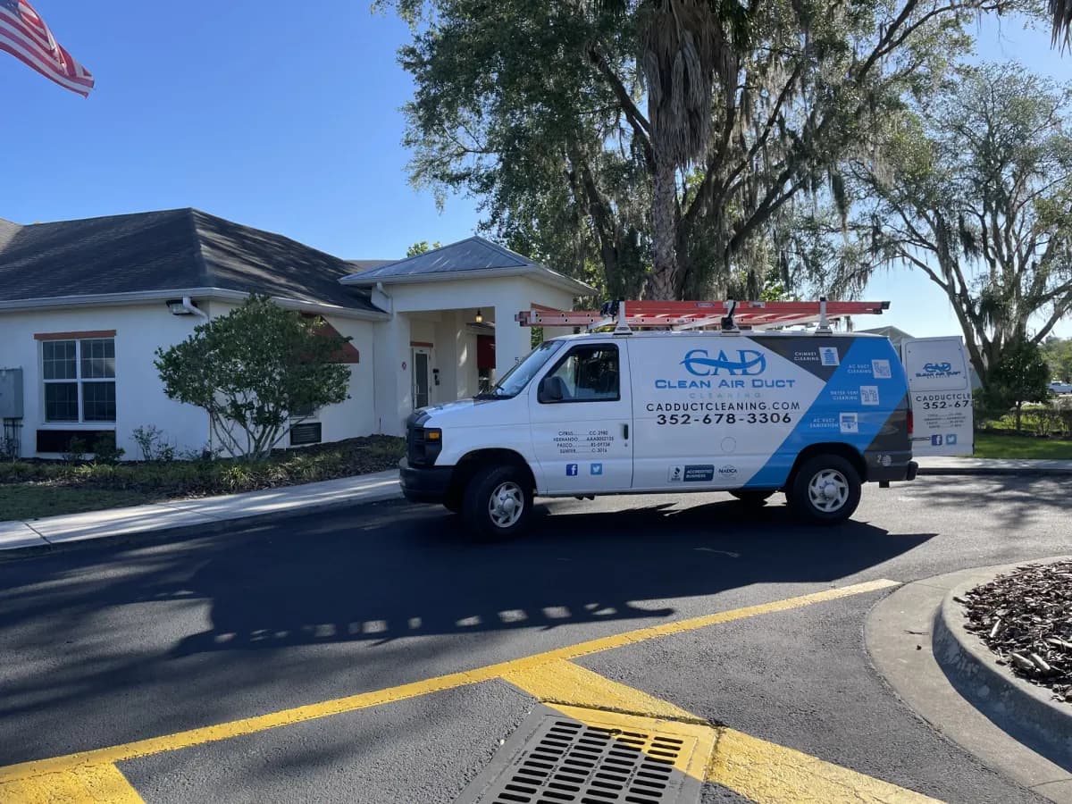 A Clean Air Duct Cleaning van parked outside a single-storey Florida home shaded by oaks and palms