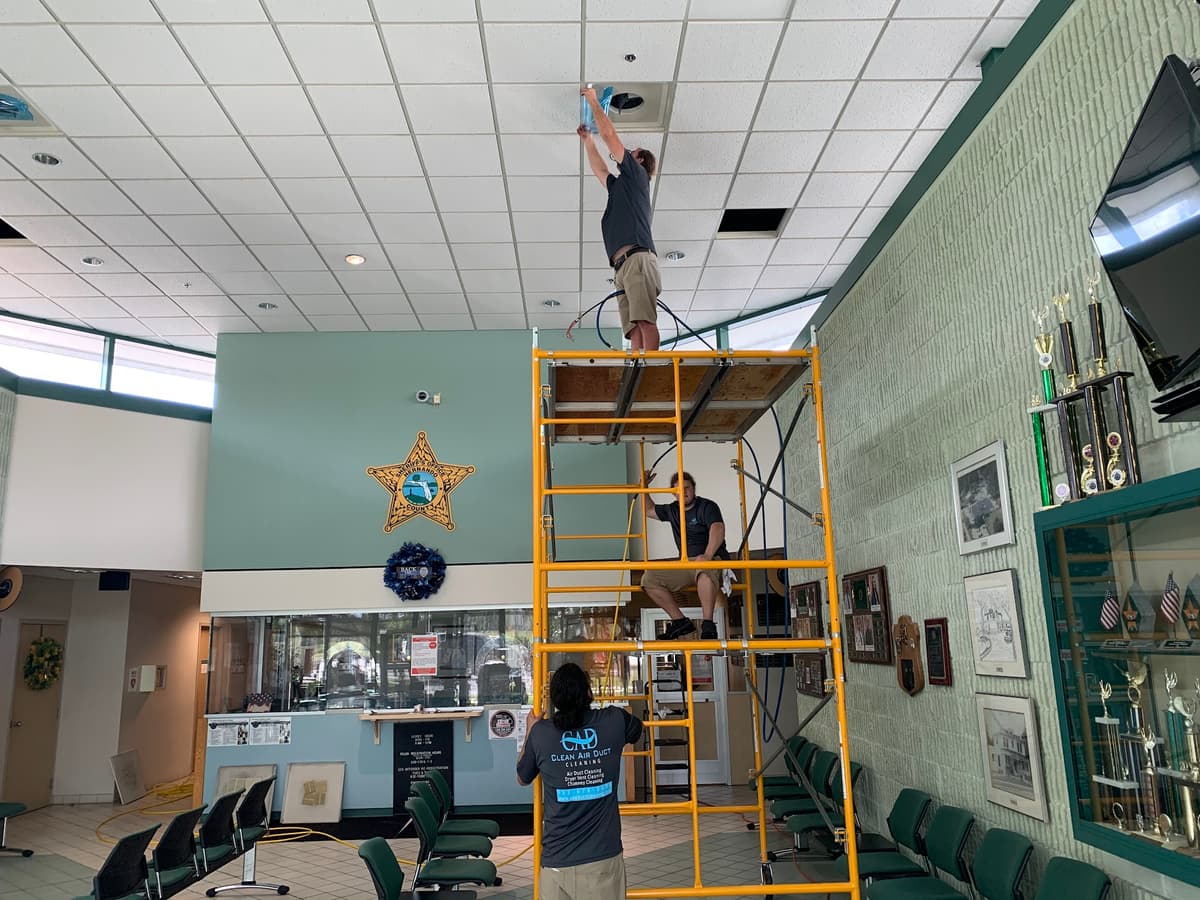 Clean Air Duct Cleaning technicians on scaffolding cleaning ceiling vents inside a Florida sheriff’s office lobby