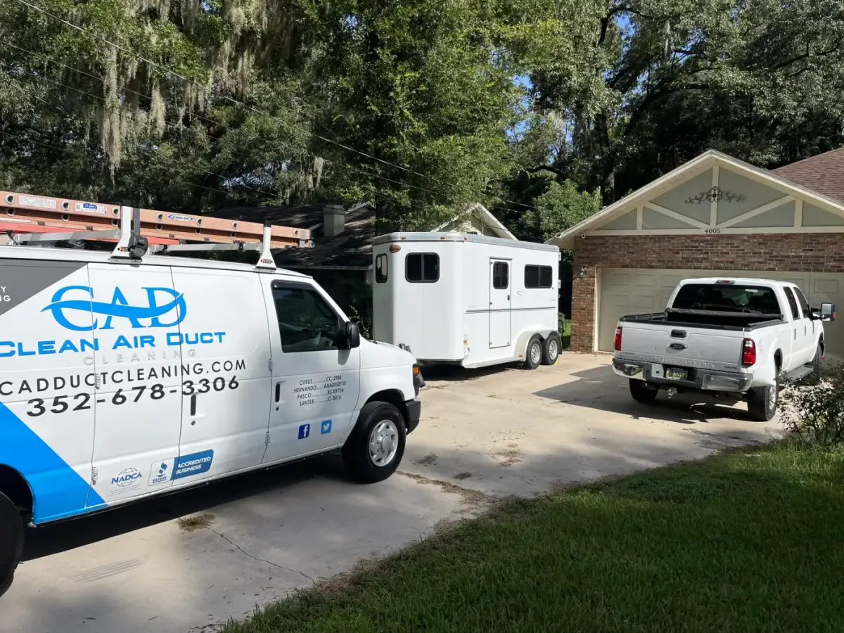 A Clean Air Duct Cleaning van and equipment trailer parked in a home driveway