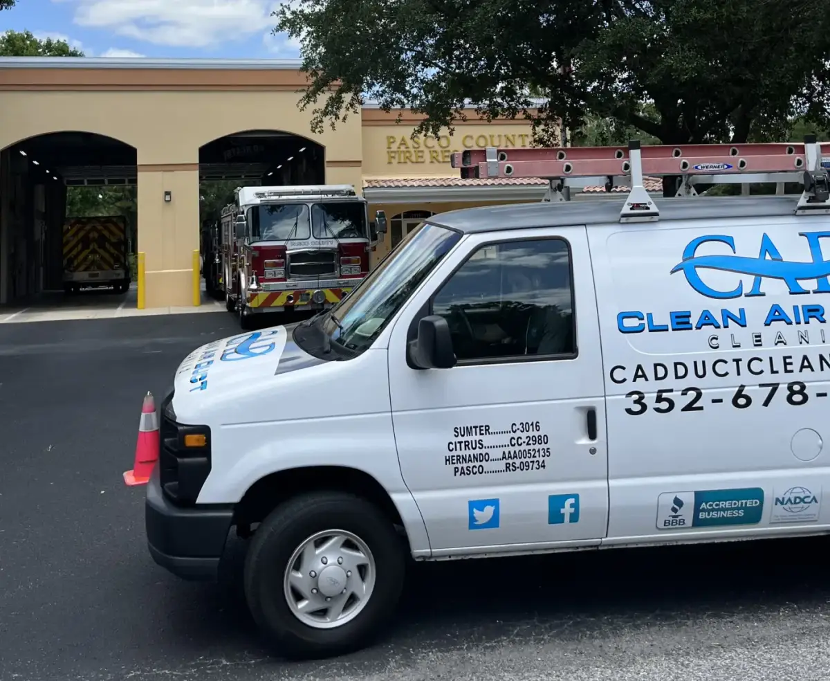 A Clean Air Duct Cleaning van parked at a fire station beside a fire engine