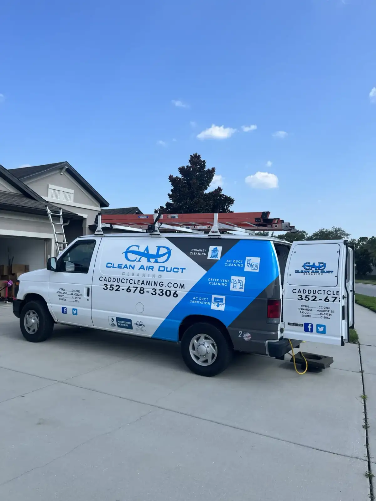 A Clean Air Duct Cleaning van with roof ladders parked in front of a home garage