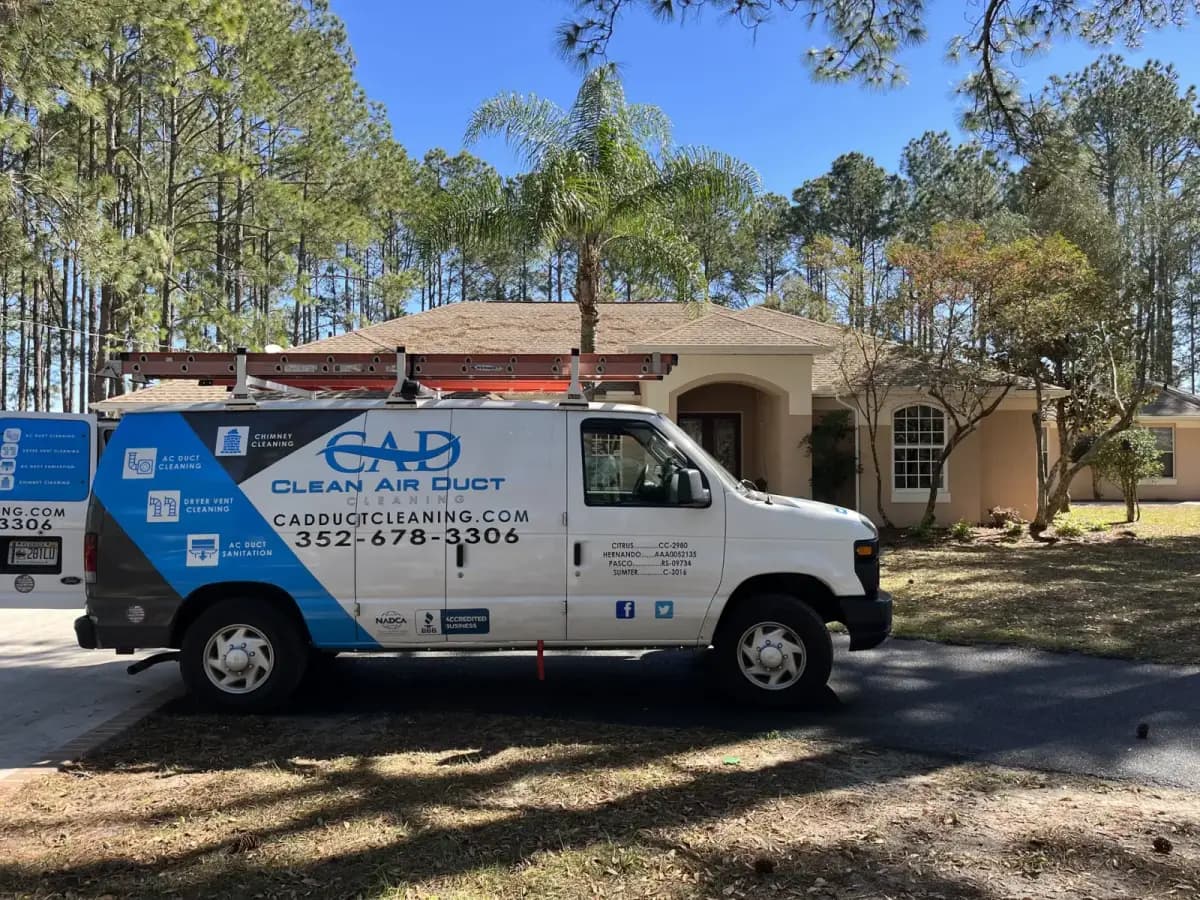 A Clean Air Duct Cleaning van outside a home surrounded by pines