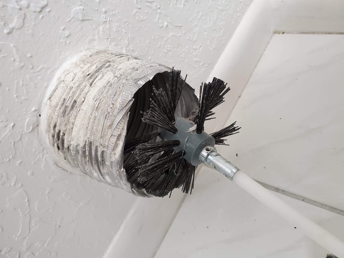A rotary brush agitating the inside of a ceiling duct run to loosen built-up debris