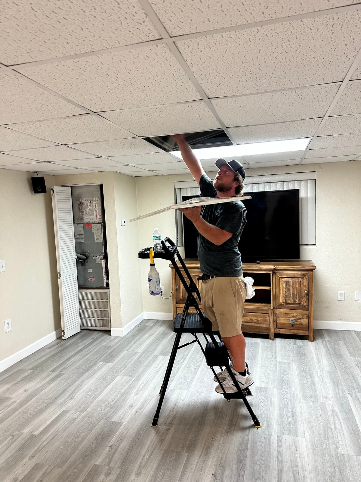 A technician cleaning a ceiling supply vent in a Central Florida living room