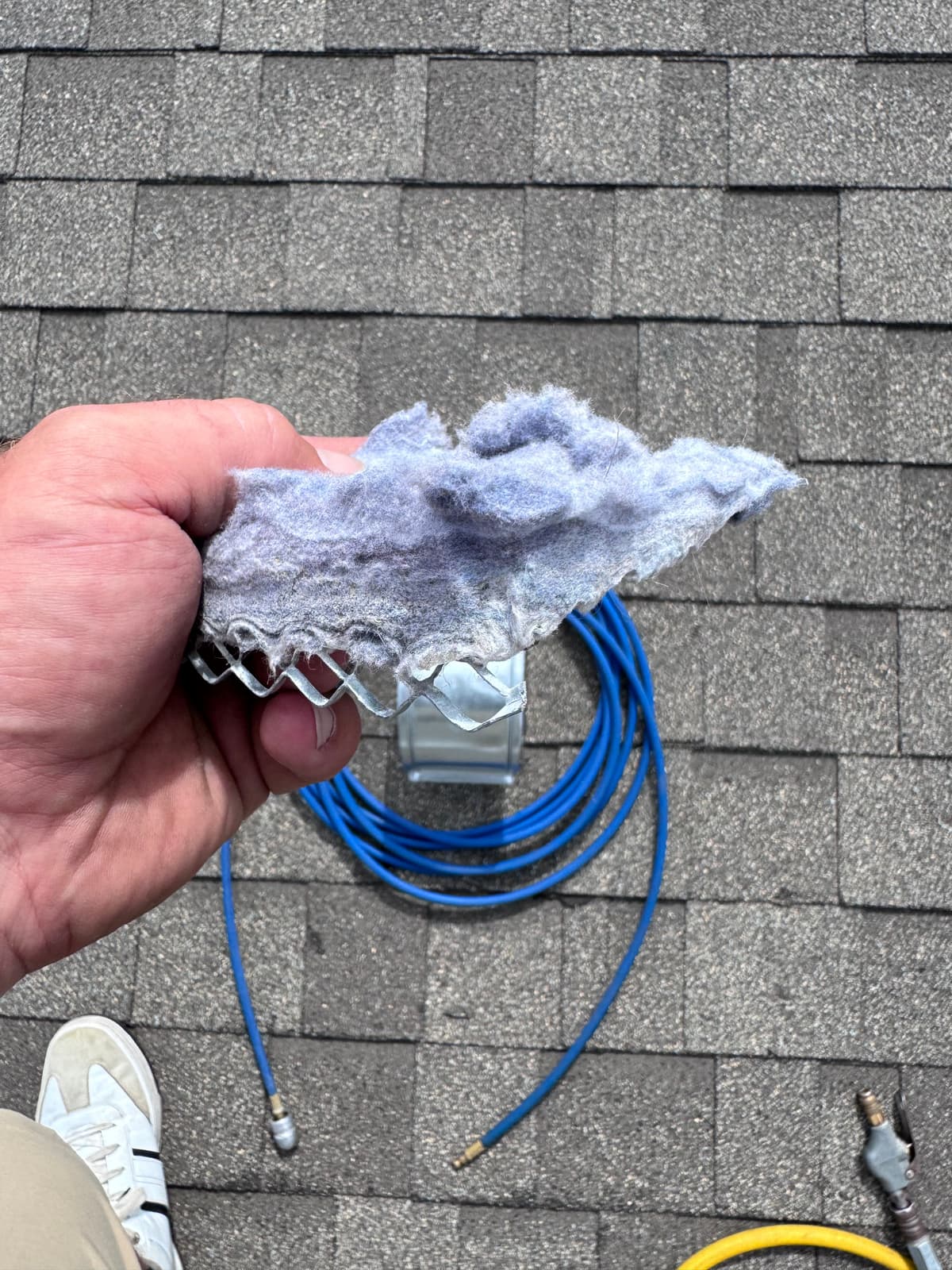 A technician holding a clump of lint pulled from a roof dryer vent screen