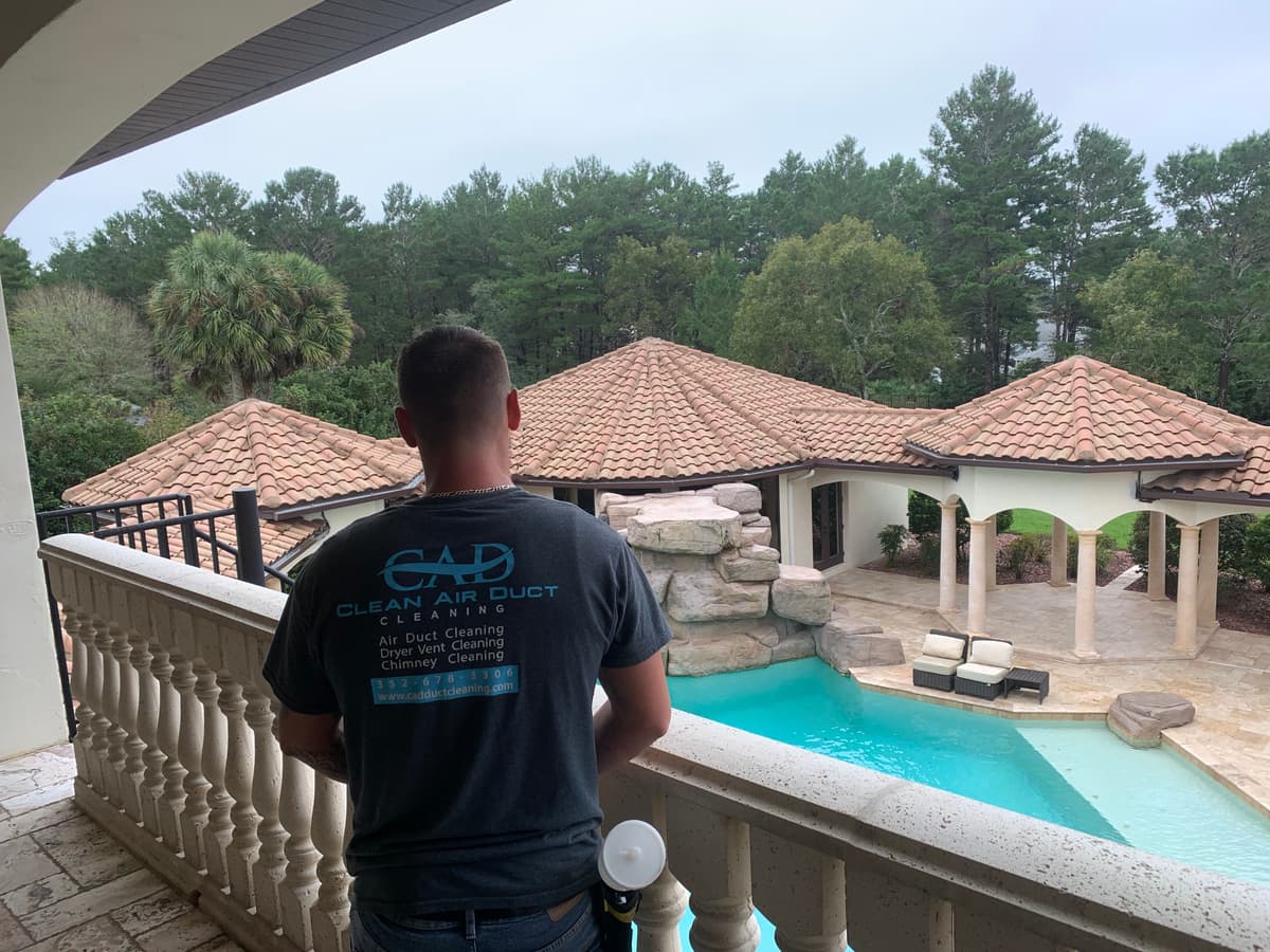 A Clean Air Duct Cleaning technician on a balcony overlooking the pool at a large residential property