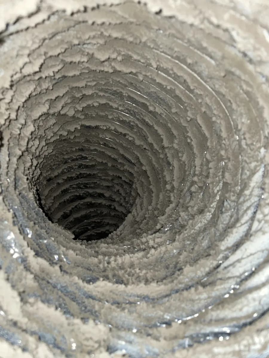 The inside of a home supply duct thickly caked with grey dust before cleaning