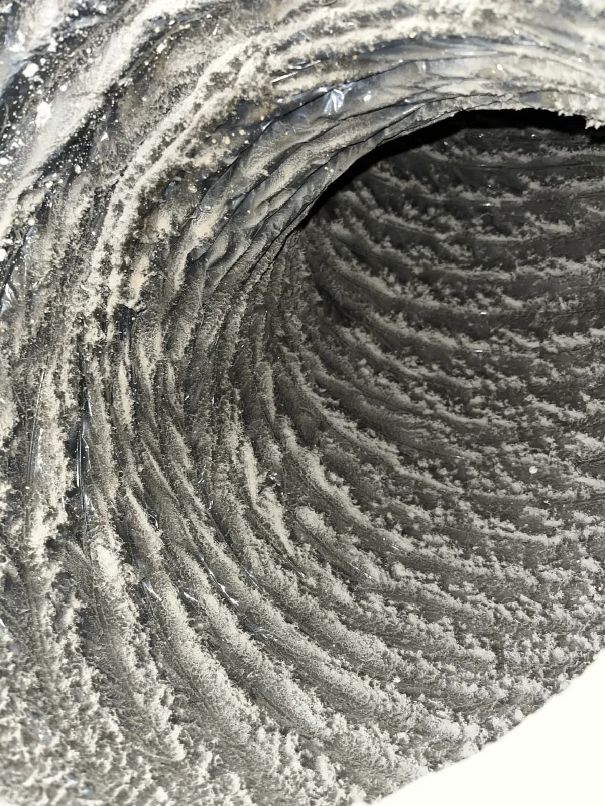 A return duct run before cleaning, its ribs packed with a thick grey coat of dust and lint