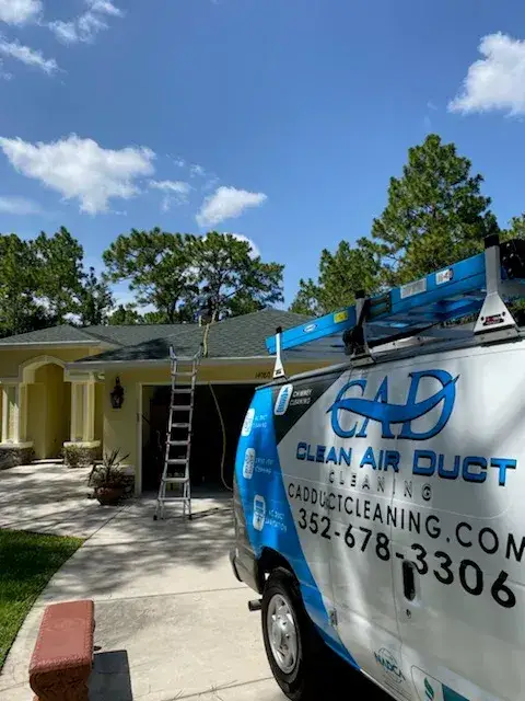 A Clean Air Duct Cleaning van with a ladder set up outside a yellow Florida home