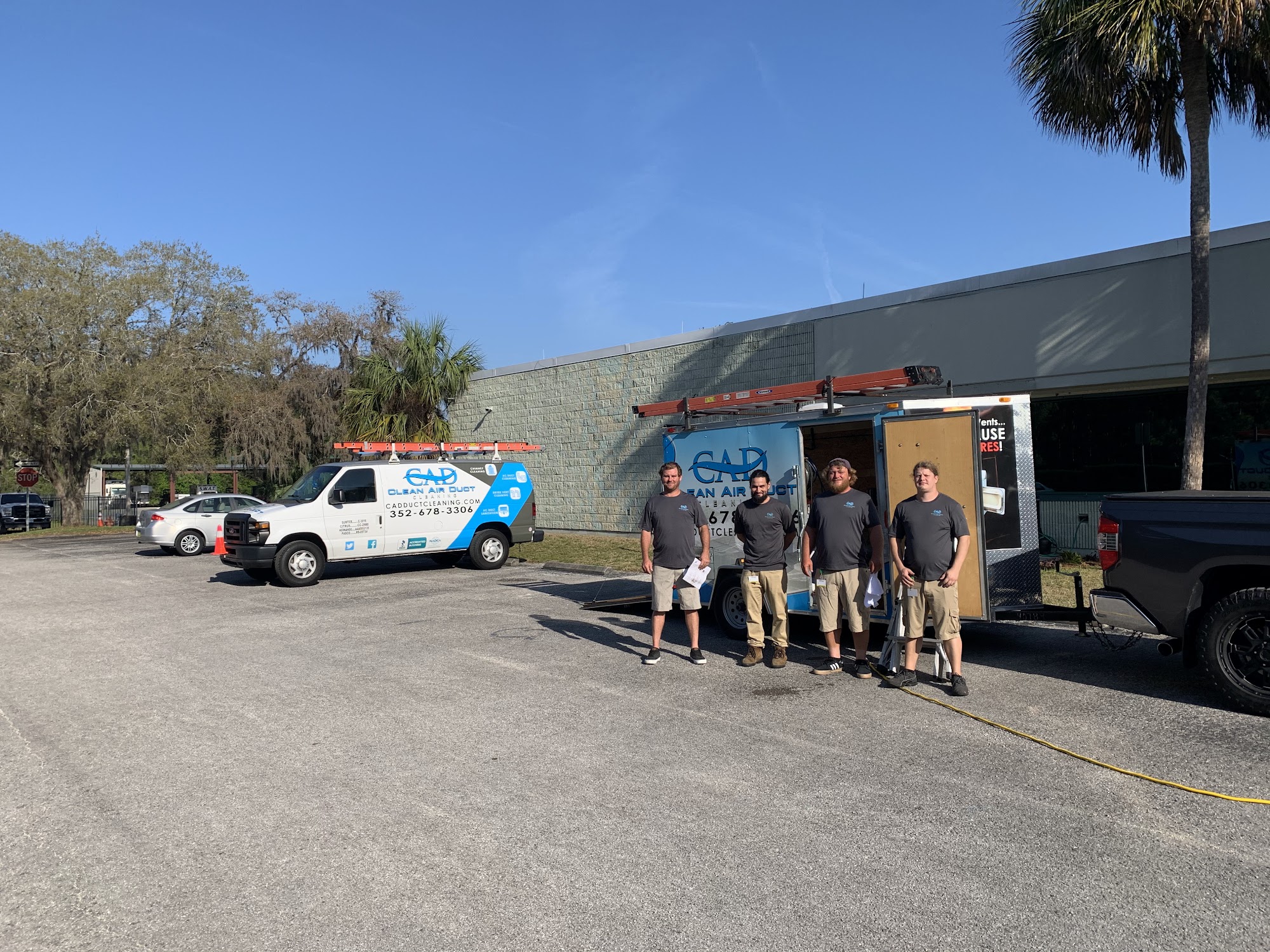 The Clean Air Duct Cleaning crew standing with their service vans outside the company workshop