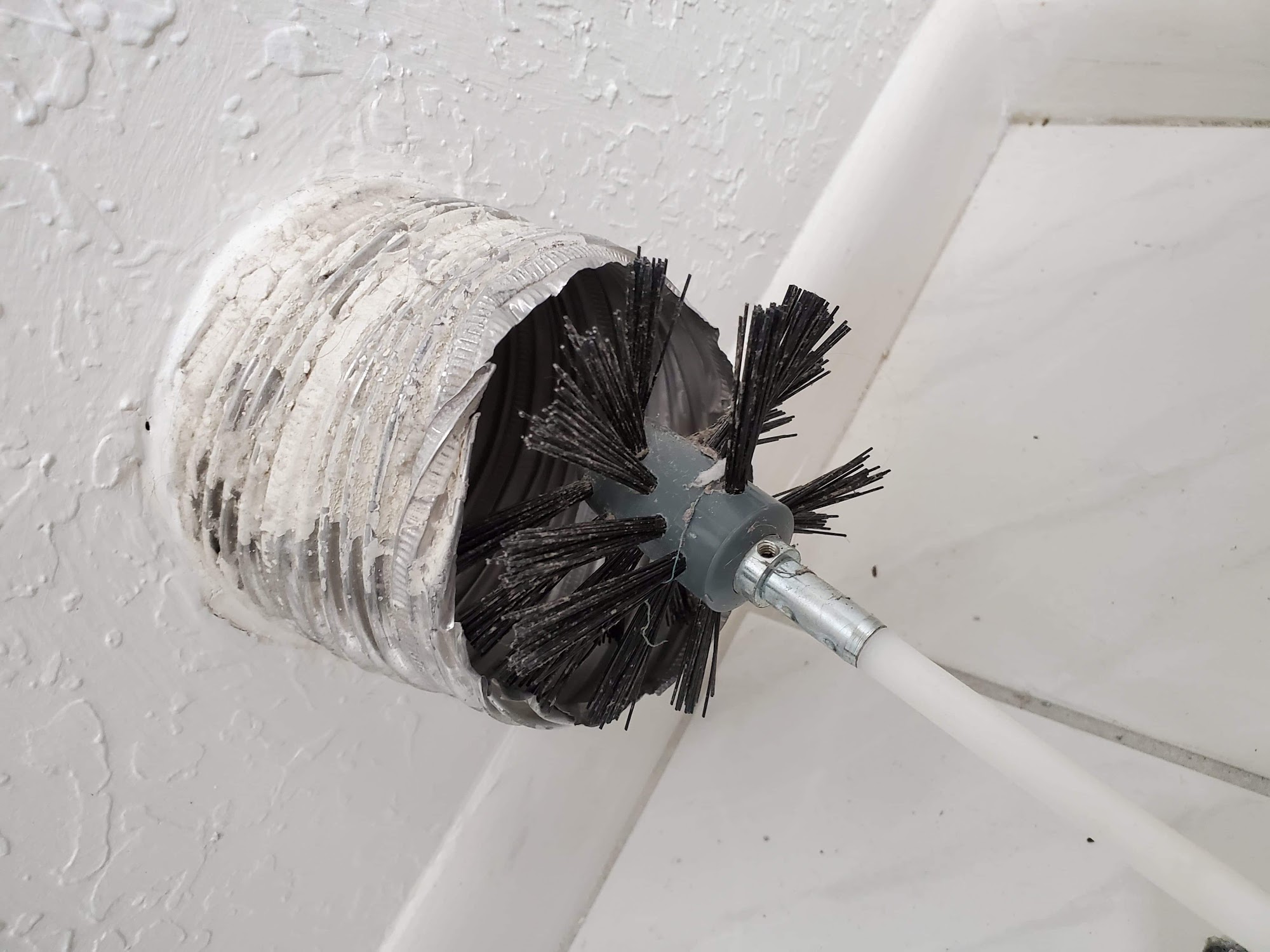 A rotary brush agitating the inside of a ceiling duct run to loosen built-up debris