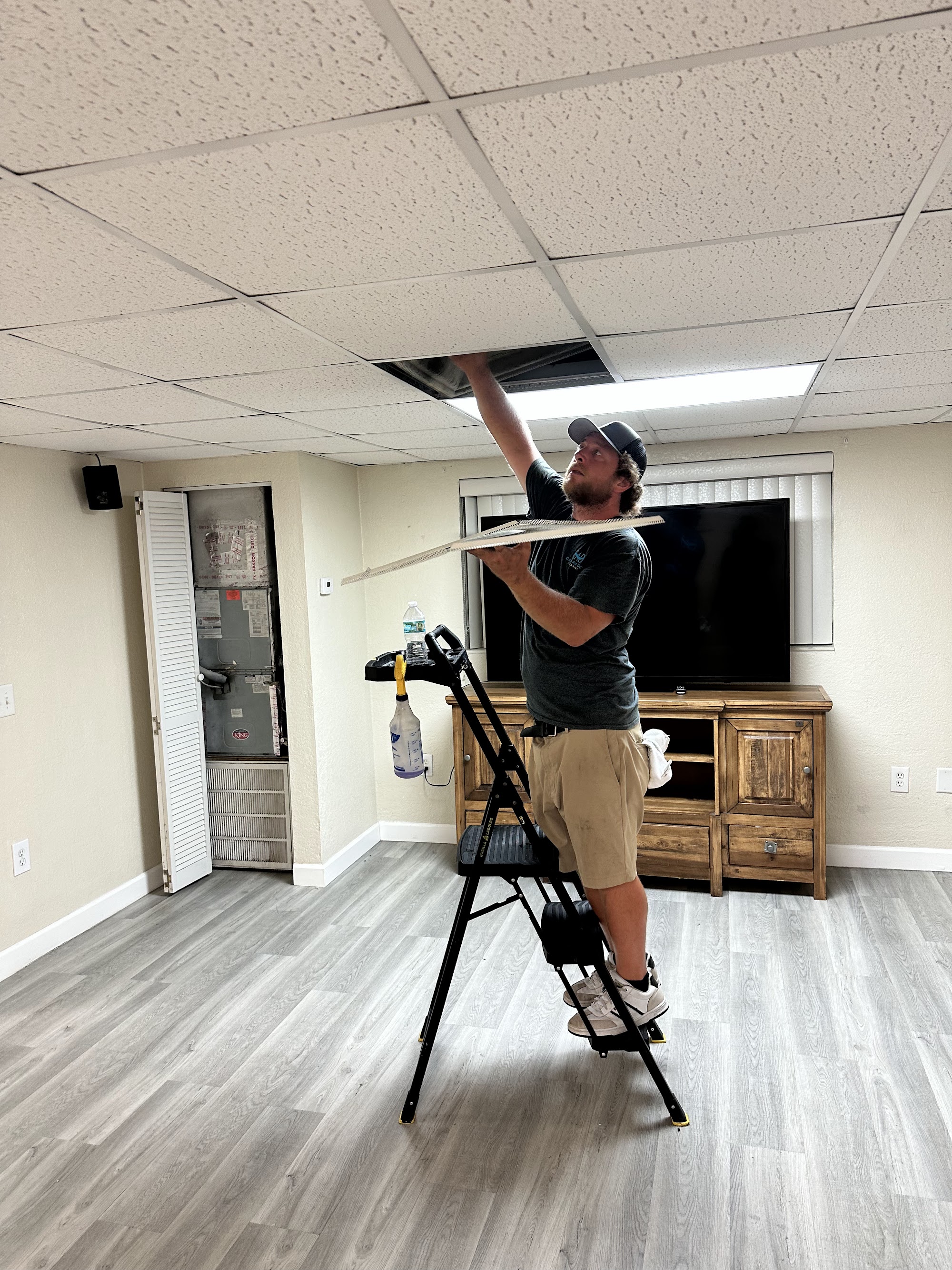 A technician cleaning a ceiling supply vent in a Central Florida living room